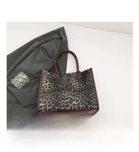 Close-up of leopard print tote bag with brown leather handles and textured canvas detail