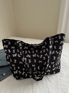 Close-up of a large black tote bag with white bow print and durable shoulder straps