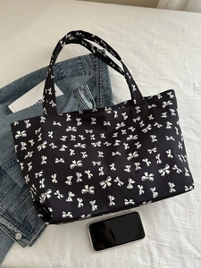 Detail view of black tote bag with white bow pattern and smooth nylon texture surface