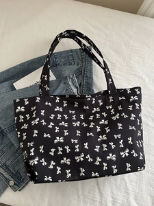Close-up of black tote bag with white bow pattern on a textured fabric background
