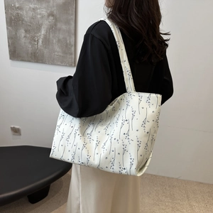 Détail d'un sac cabas en toile blanche à motifs floraux bleus porté par un mannequin
