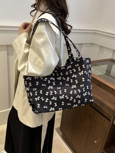 Side view of large tote bag with black and white bow print on model in elegant indoor setting