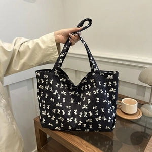 Large black tote bag with white bow pattern and long straps for shoulder or hand carry