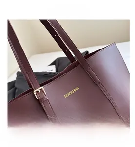 Close-up of dark burgundy tote bag featuring adjustable gold buckle and brand lettering