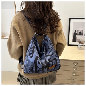 Close-up of navy canvas backpack with black graffiti prints and brown leather logo tag