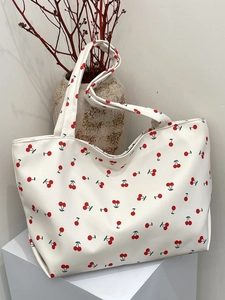 Détail d'un sac cabas en toile blanche avec imprimés cerises sur un support minimaliste