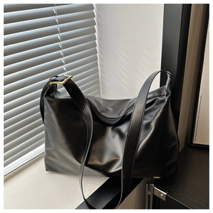 Close-up of matte black leather tote bag with wide strap and golden square buckle detail