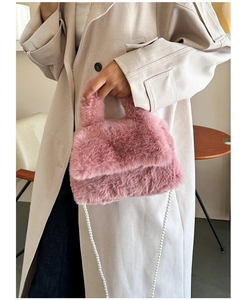 Détail d'un sac en fausse fourrure rose avec chaîne en perles porté sur un trench-coat beige