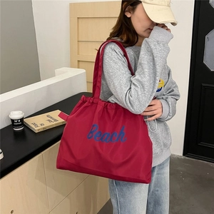 Large burgundy nylon tote bag with blue Beach lettering shown on a female model