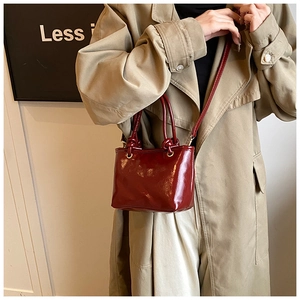 Detail of burgundy patent leather handbag with gold hardware styled on khaki trench coat