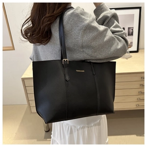 Detail of a large black leather tote bag featuring gold fashion lettering and long strap