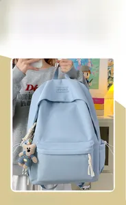Detail of light blue nylon backpack featuring a cute teddy bear plush charm attachment