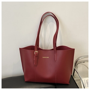 Detail of burgundy tote bag with gold lettering and metal buckle on leather bench