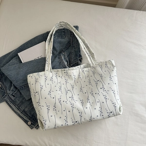 Détail du sac cabas en toile blanche aux motifs de feuilles noires sur veste en jean