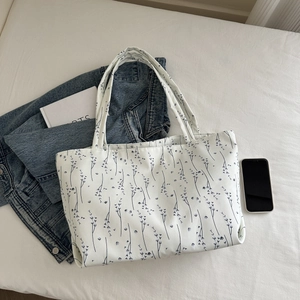 Vue à plat d'un sac cabas blanc à fleurs bleues avec une veste en jean et un livre blanc