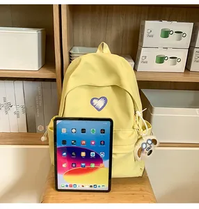Detail of yellow canvas backpack showing violet heart logo and plush puppy keychain