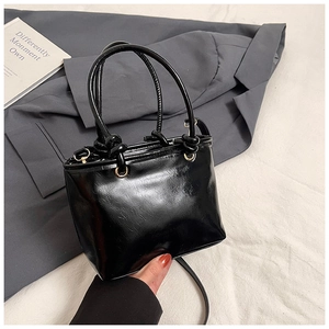 Detail of black patent leather bucket bag with gold hardware and knotted handle design