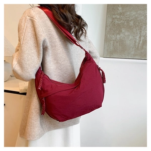 Détail du sac bandoulière croissant en nylon bordeaux porté par un mannequin en intérieur