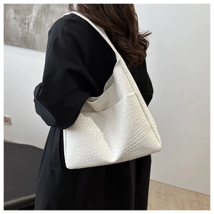 Detail of white woven tote bag shown on a model's shoulder against a black coat