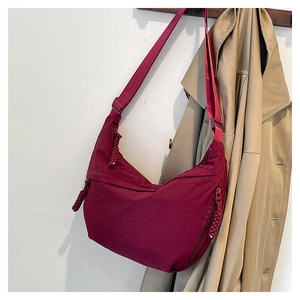 Détail du sac croissant bordeaux en nylon avec breloque tissée et bandoulière large