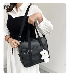 Detail of black PU leather JK uniform bag featuring a cute white plush bear charm