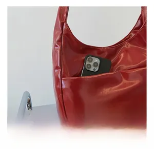 Detail of red glossy hobo bag featuring a functional front pocket for smartphone storage