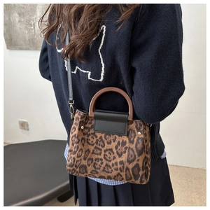 Detail of leopard print handbag featuring wooden handles and adjustable black shoulder strap