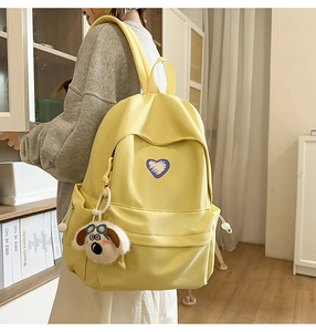 Detail of a bright yellow canvas backpack featuring a purple heart patch and a plush dog charm