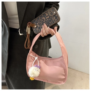 Pink crescent hobo bag with white plush charm held in hand with green jacket