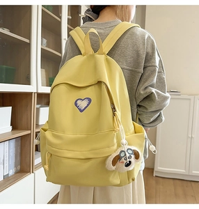 Detail of light yellow canvas backpack with purple heart embroidery and plush dog charm