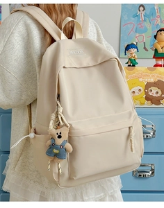 Detail of light beige nylon backpack featuring front flap pocket and cute bear plush charm