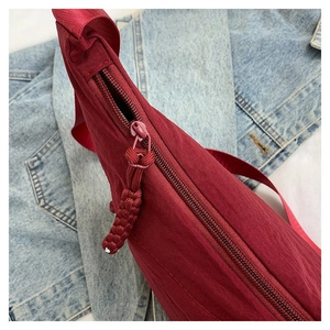 Détail du sac à bandoulière demi-lune rouge foncé avec fermeture éclair à nœud tressé
