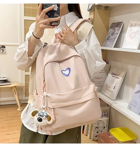 Detailed side view of pink backpack with blue heart and plush pendant in school setting