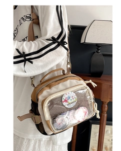 Détail d'un sac Ita beige avec fenêtre transparente montrant des badges d'anime