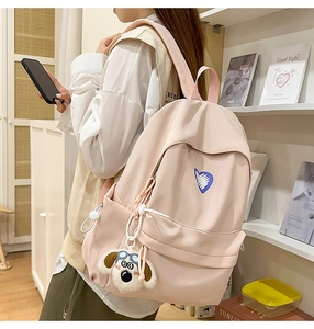 Detail of light pink student backpack with heart embroidery and cartoon puppy charm