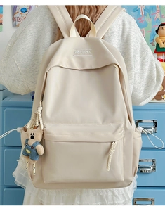 Detail of a beige campus backpack with a front zipper pocket and a cute bear plush charm