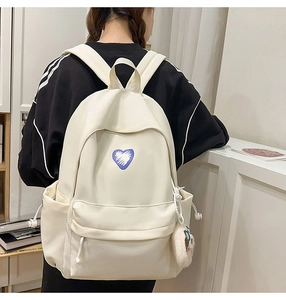 Close-up of off-white minimalist backpack with purple heart patch and plush charm