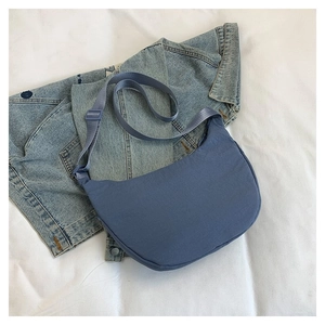 Détail du sac demi-lune en toile bleue avec bandoulière réglable sur fond textile