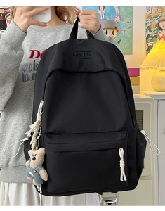 Detail of black nylon backpack with XINFEIDA embroidery and cute beige bear pendant