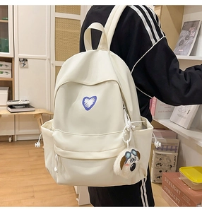 Detail of white nylon backpack featuring a blue heart patch and cute dog plush charm