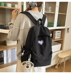 Detail of black nylon backpack with blue heart patch and cute plush dog charm