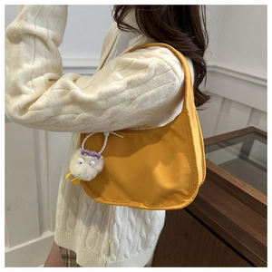 Bright yellow half-moon nylon bag with cartoon pendant worn over casual knitwear