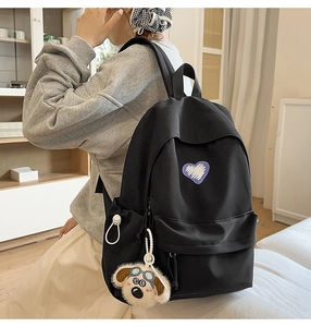 Detailed side view of black canvas backpack with heart embroidery and dog plush charm