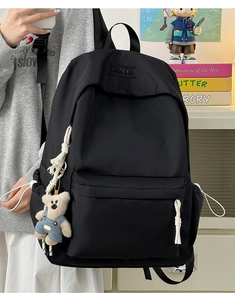 Detail of black nylon backpack with multi-pocket design and cute teddy bear pendant charm