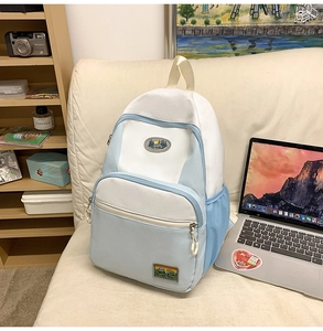 Detail of light blue nylon backpack with vintage mountain patches on white sofa