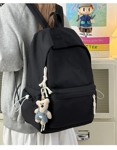 Close-up of black nylon backpack featuring white woven rope zipper pulls and a plush bear charm