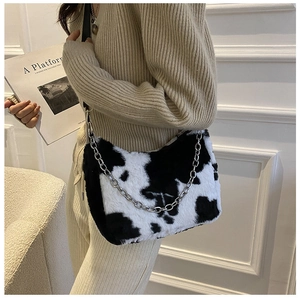Detail of plush cow print shoulder bag with silver chain strap on beige knit outfit