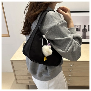 Minimalist black nylon crescent shoulder bag with white plush charm shown on model