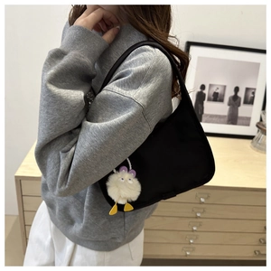 Detail of minimalist black nylon hobo bag with a cute white plush monster charm on the side