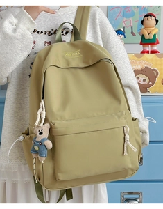 Detail of khaki nylon backpack featuring front zipper pocket and plush bear charm decoration